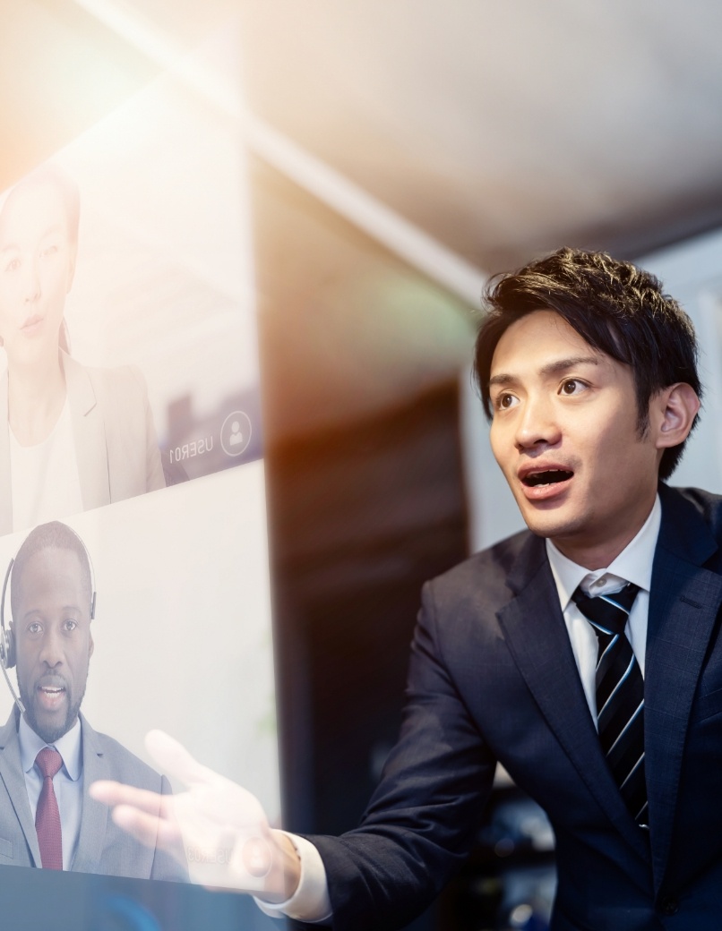 写真：オンラインビデオ会議中のアジア人ビジネスマン。画面には黒人男性の同僚が映っている