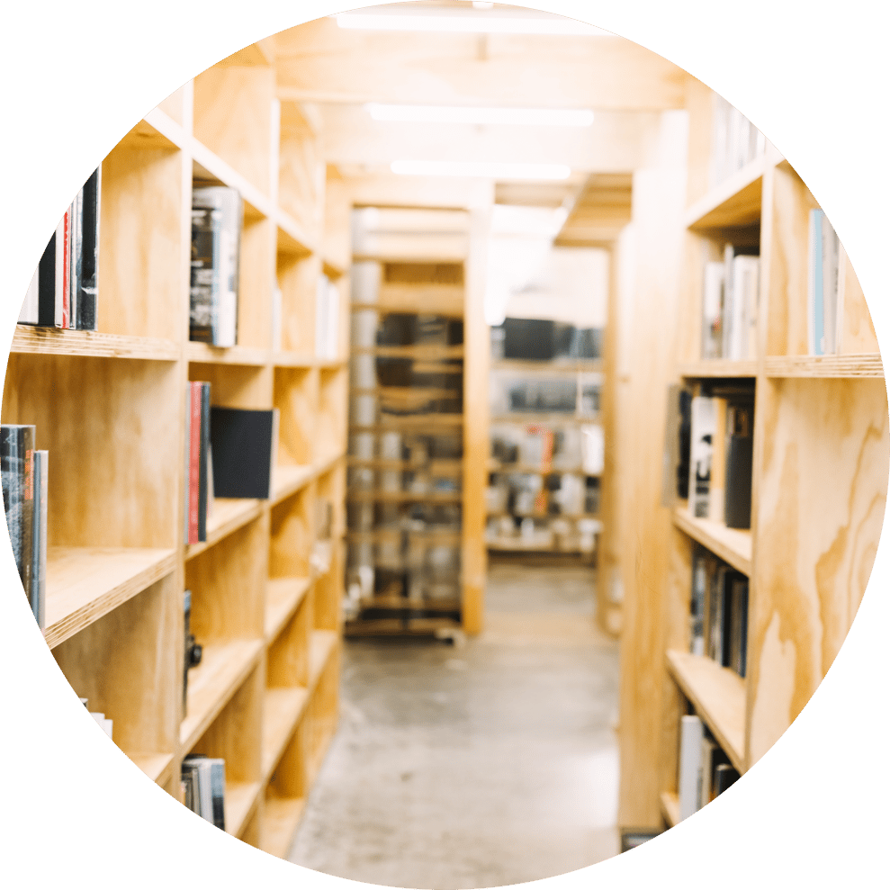 写真：木製の本棚が並ぶ図書館の通路。明るい木目の棚に多数の本が並んでいる様子
