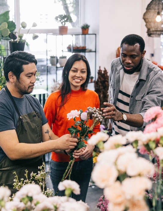 写真：3人が花屋で花を選んでいるシーン。