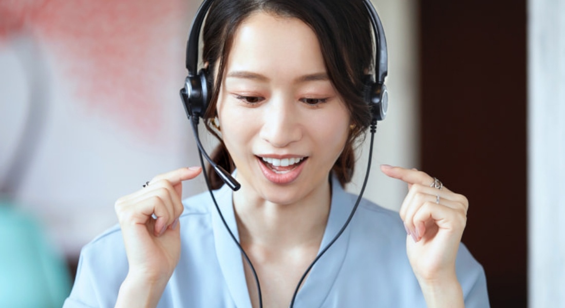 写真：ヘッドセットを着けて英語の発音練習を行う女性。真剣な表情で発音を確認している。