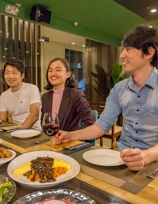 写真：夕食の場でリラックスした雰囲気の生徒たちが、笑顔で食事を楽しんでいる。テーブルには多彩な料理が並べられている。