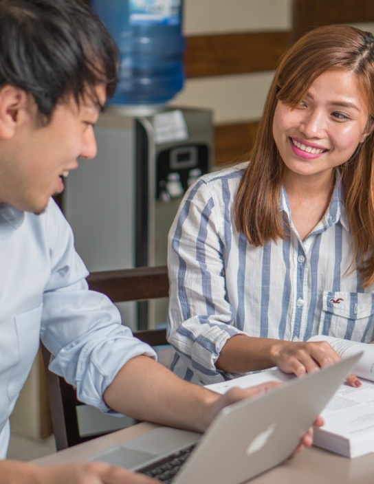 写真：学習資料を見ながら会話をする男女。明るい笑顔と親しみやすい雰囲気が印象的な教室内の一場面。